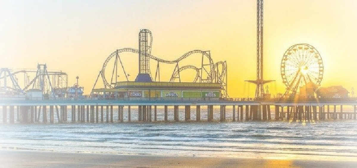The beach with a pier going out into the ocean with an amusement park on it.