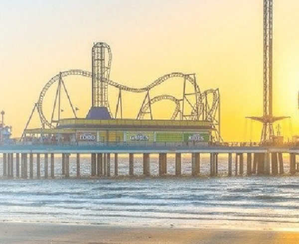 The beach with a pier going out into the ocean with an amusement park on it.